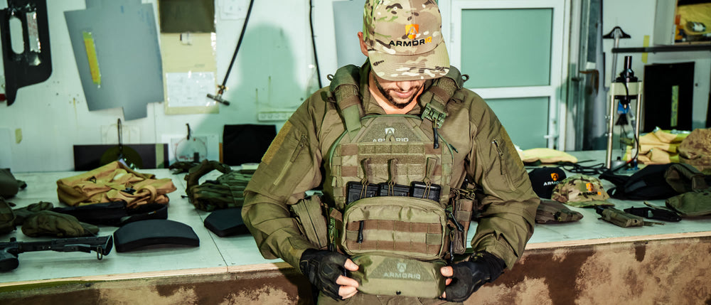 Fitting an ArmorIQ plate carrier in the workshop, with armor plates on the bench behind